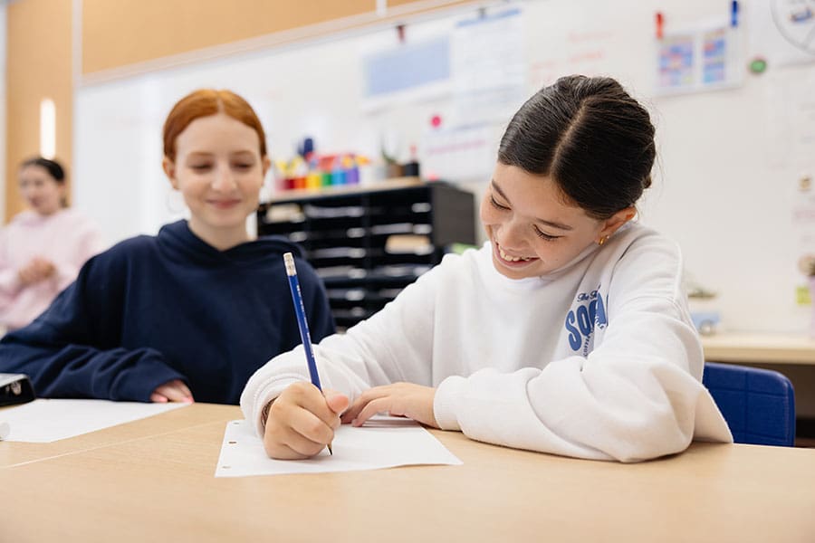 Student Academics - two students in a classroom, one is writing
